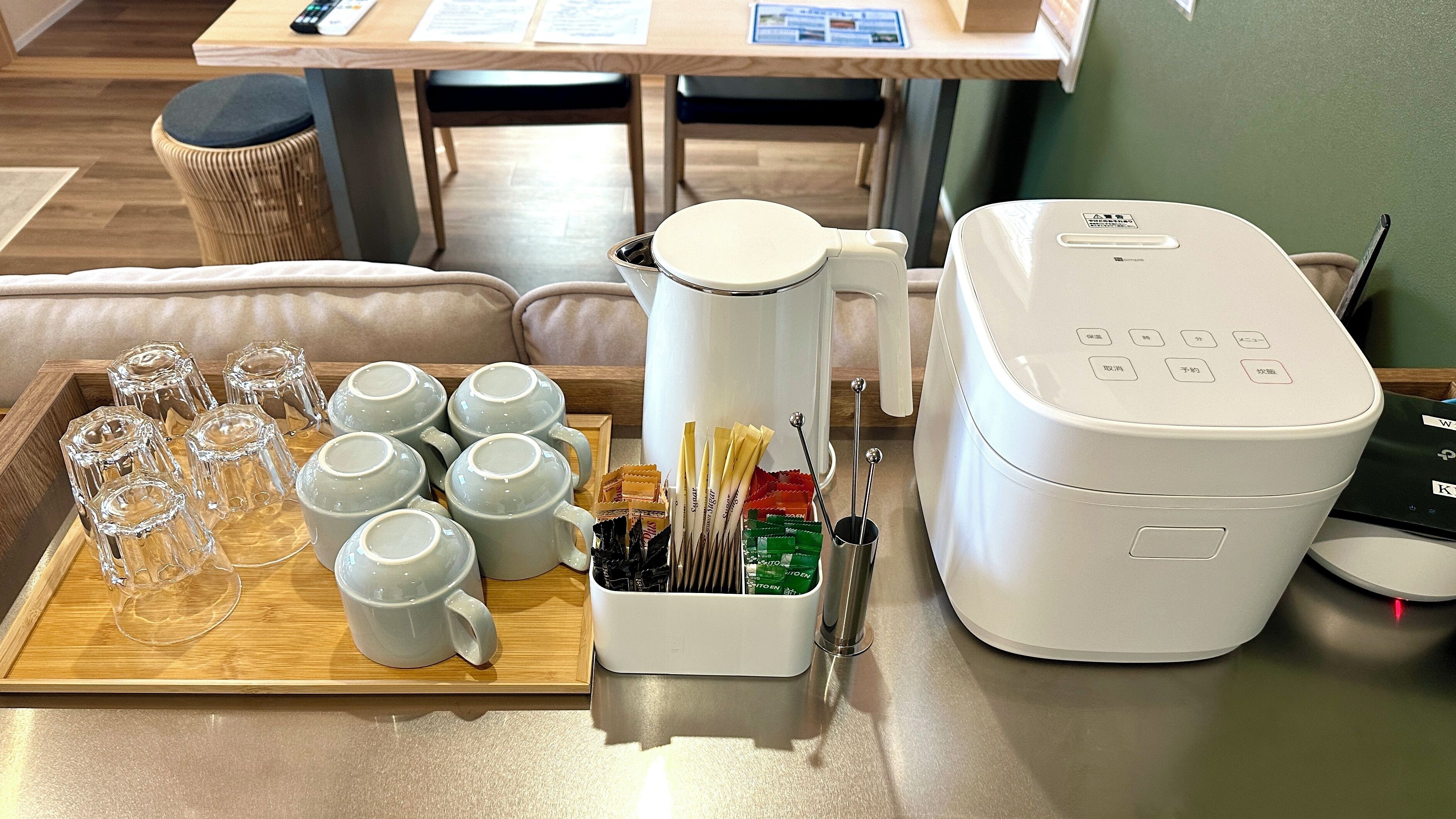 Una bandeja con tazas de vidrio transparente, una tetera eléctrica blanca y un recipiente con bolsitas de té y utensilios.