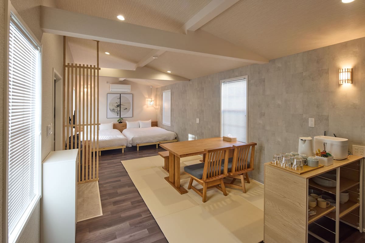 A modern interior with a wooden dining table, chairs, a sofa, and a kitchen area with cabinets and appliances.