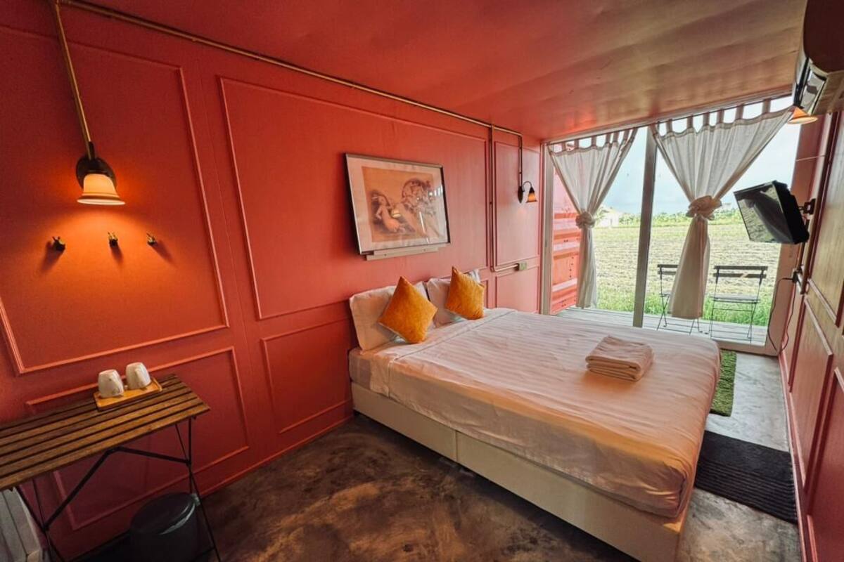 A bedroom with a bed, pillows, a table with cups, and a painting on the wall.