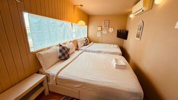 A bedroom with two beds, a bench, a wall-mounted TV, and a window with a curtain.