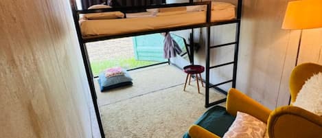 Habitación compacta con literas, un sillón amarillo, una mesita y una lámpara.