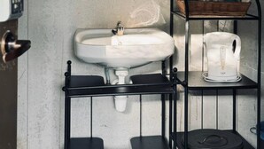 A bathroom with a white sink, a round mirror, and a metal shelf holding toiletries. - Padi Box (Sekinchan)