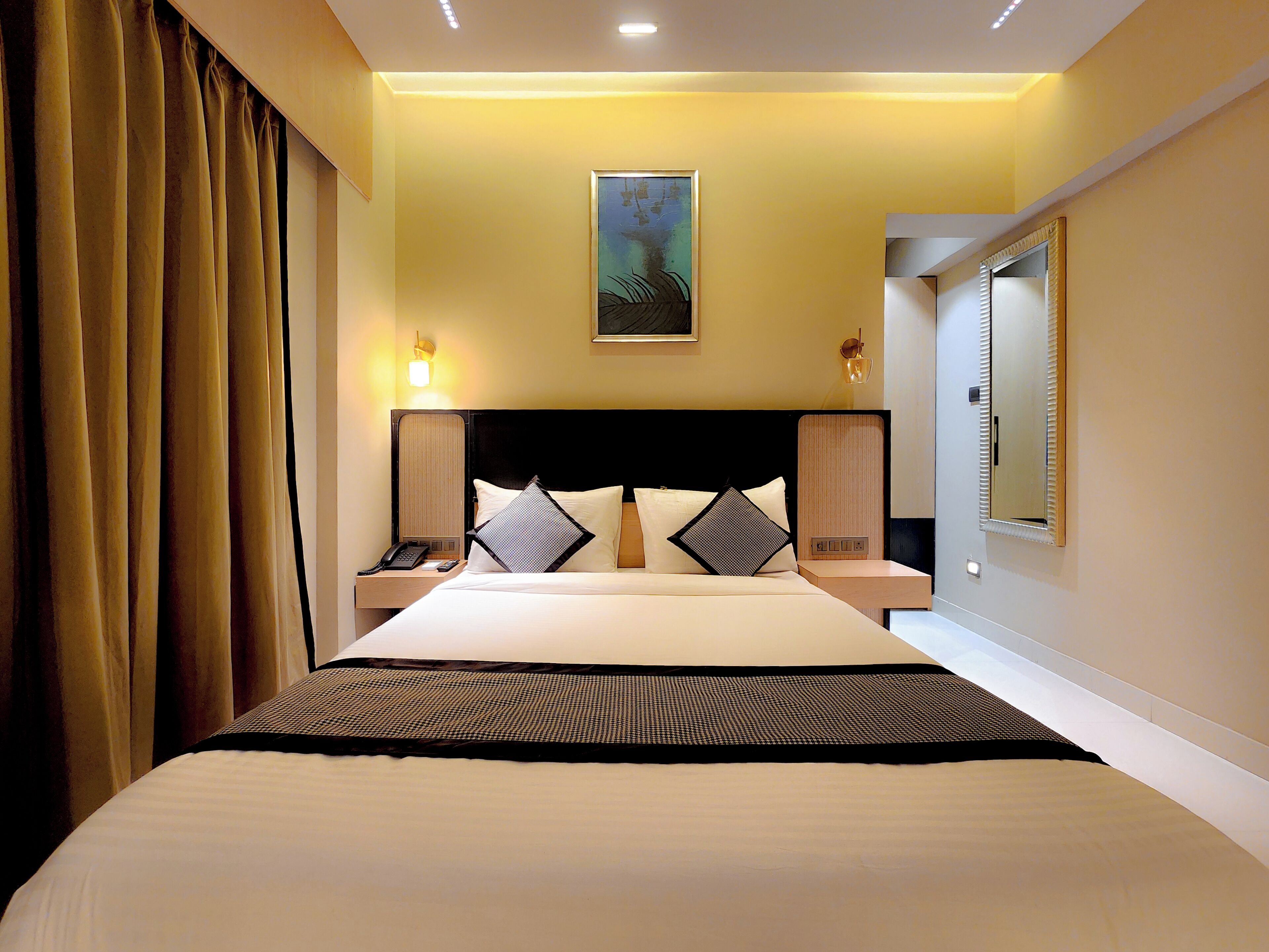 Une chambre d’hôtel avec un grand lit, des lampes de chevet, un tableau au mur et une fenêtre avec des stores.