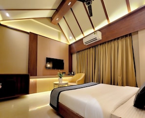 A modern hotel room with a large bed, a flat-screen TV, a small table with a plant, and a sofa.