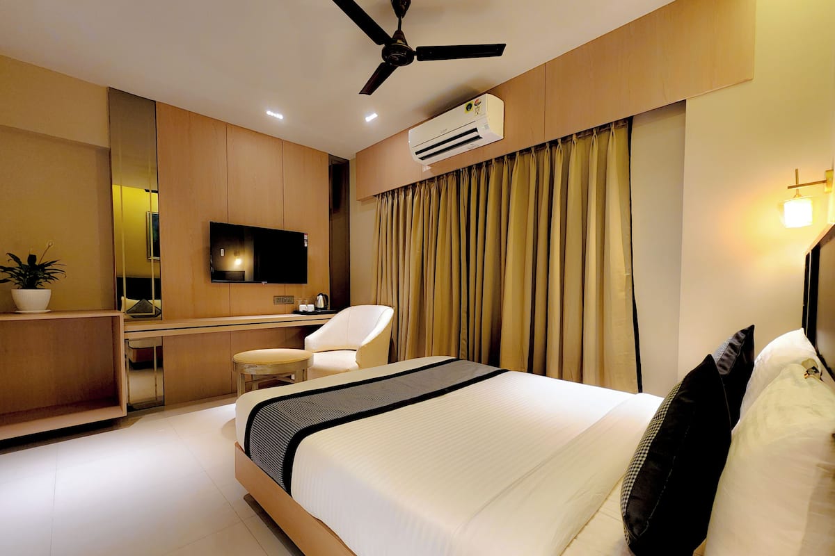 A modern hotel room with a bed, a desk, a chair, a television, an air conditioning unit, and a ceiling fan.