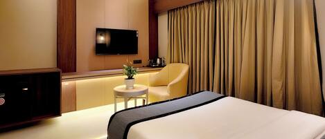 Una habitación de hotel con una cama grande, un ventilador de techo, un equipo de aire acondicionado, un televisor, una mesita con una planta y un sofá.
