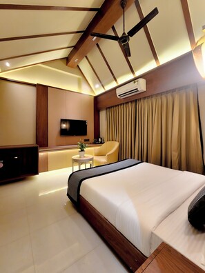 A hotel room with a large bed, a ceiling fan, an air conditioning unit, a TV, a small table with a plant, and a sofa.