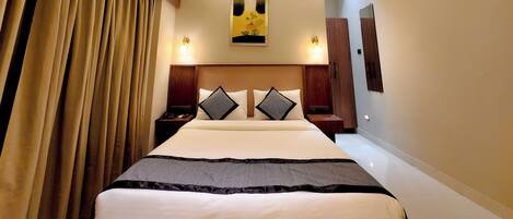 Ein Hotelzimmer mit Bett, Deckenventilator, Kunstwerken, Nachttischlampen und einem Kleiderschrank.