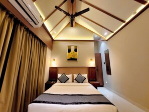 A hotel room with a bed, ceiling fan, artwork, bedside lamps, and a wardrobe.