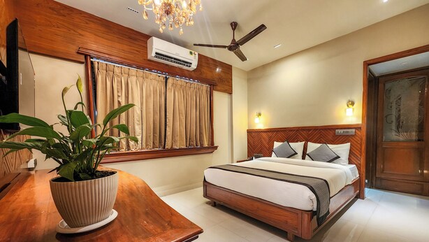 Une chambre d’hôtel avec un lit en bois, un ventilateur de plafond, un appareil de climatisation, une plante en pot et un bureau en bois.