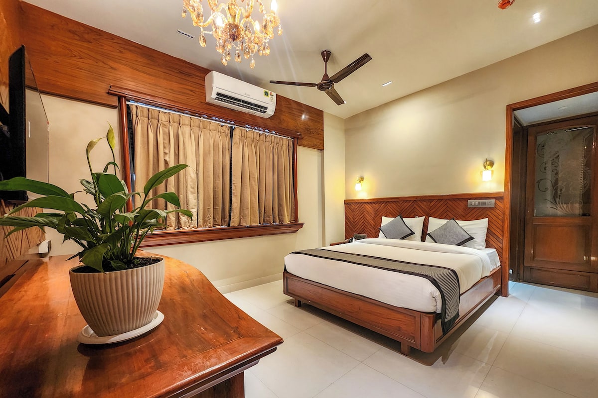 A hotel room with a wooden bed, a ceiling fan, an air conditioning unit, a potted plant, and a wooden desk.