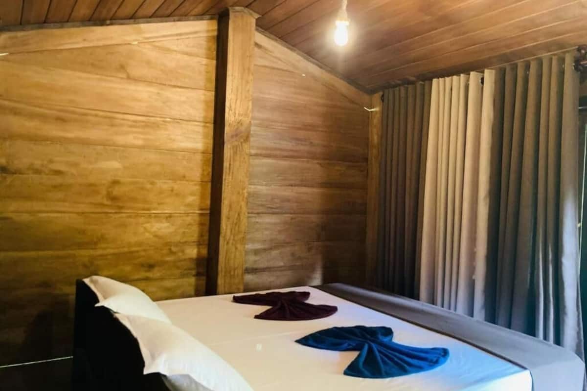 Una habitación de madera con una cama, una ventana con cortinas y una lámpara.