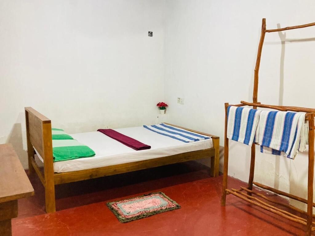 A small, single-bed room with a wooden bed frame, a red floor, a small rug, and a wooden drying rack with clothes.