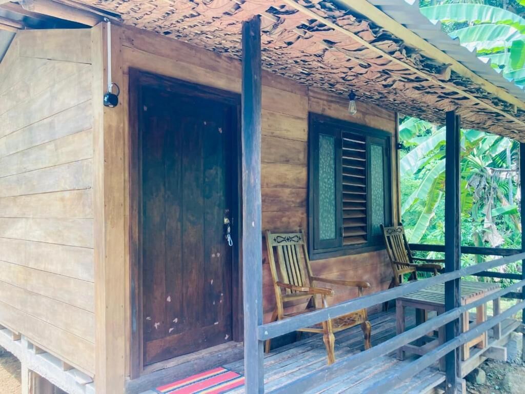 A wooden cabin with a porch, two wooden chairs, and a door.