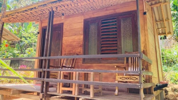 Una cabaña de madera con porche, contraventanas de madera y una pequeña mesa.