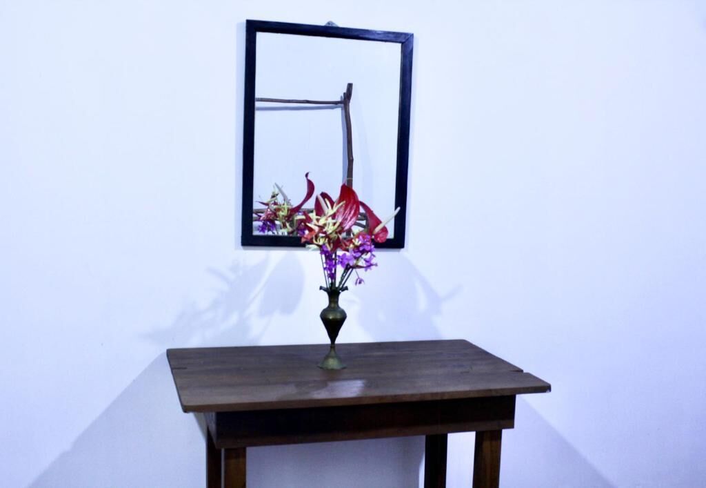 A table with a vase of flowers and a framed picture on the wall behind it.