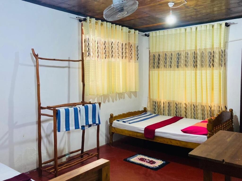 Una cama individual con cabecera de madera, una mesa de madera, un ventilador y una ventana con cortinas estampadas.