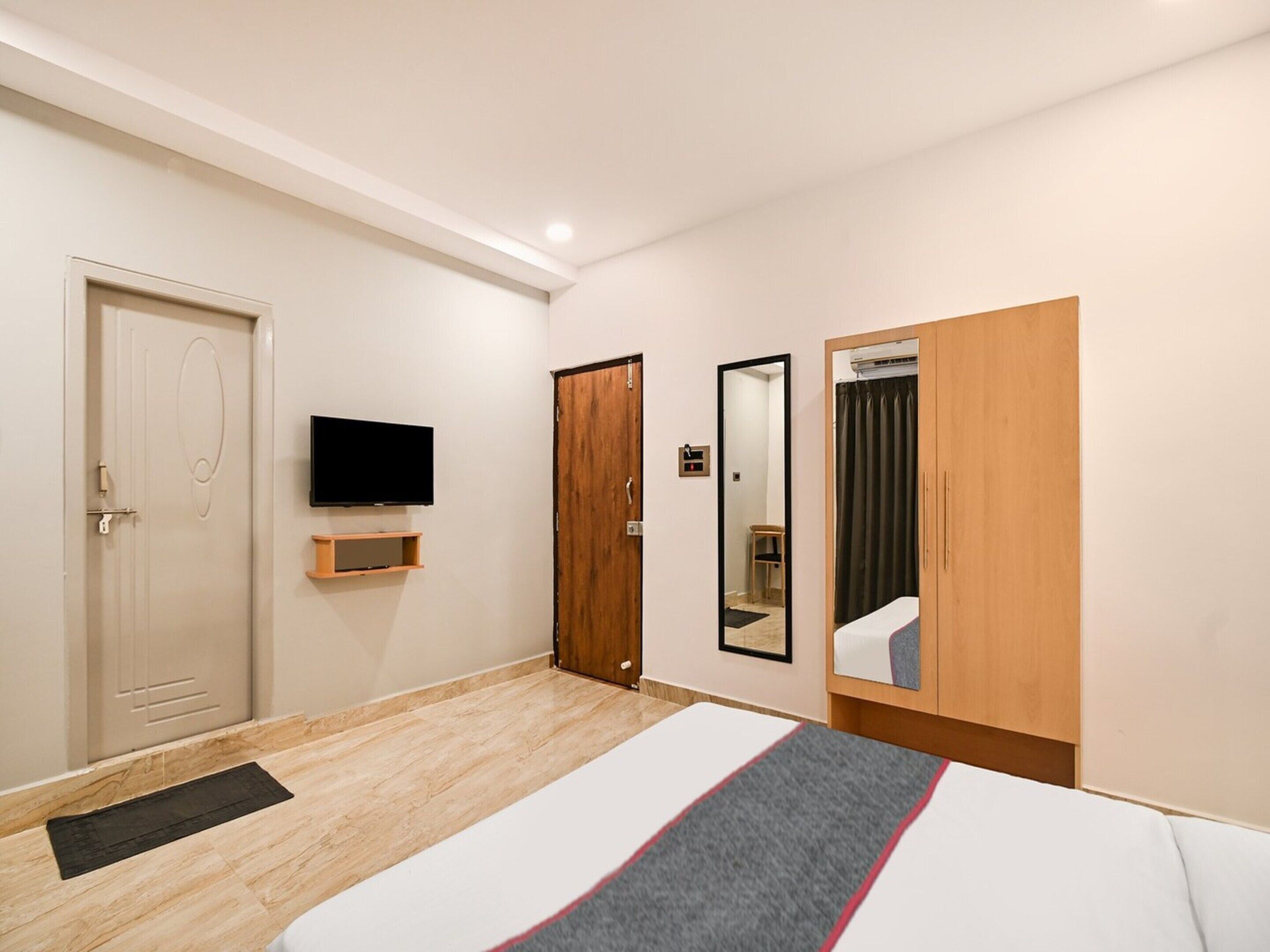A hotel room with a bed, a television, a wardrobe, and a mirror.