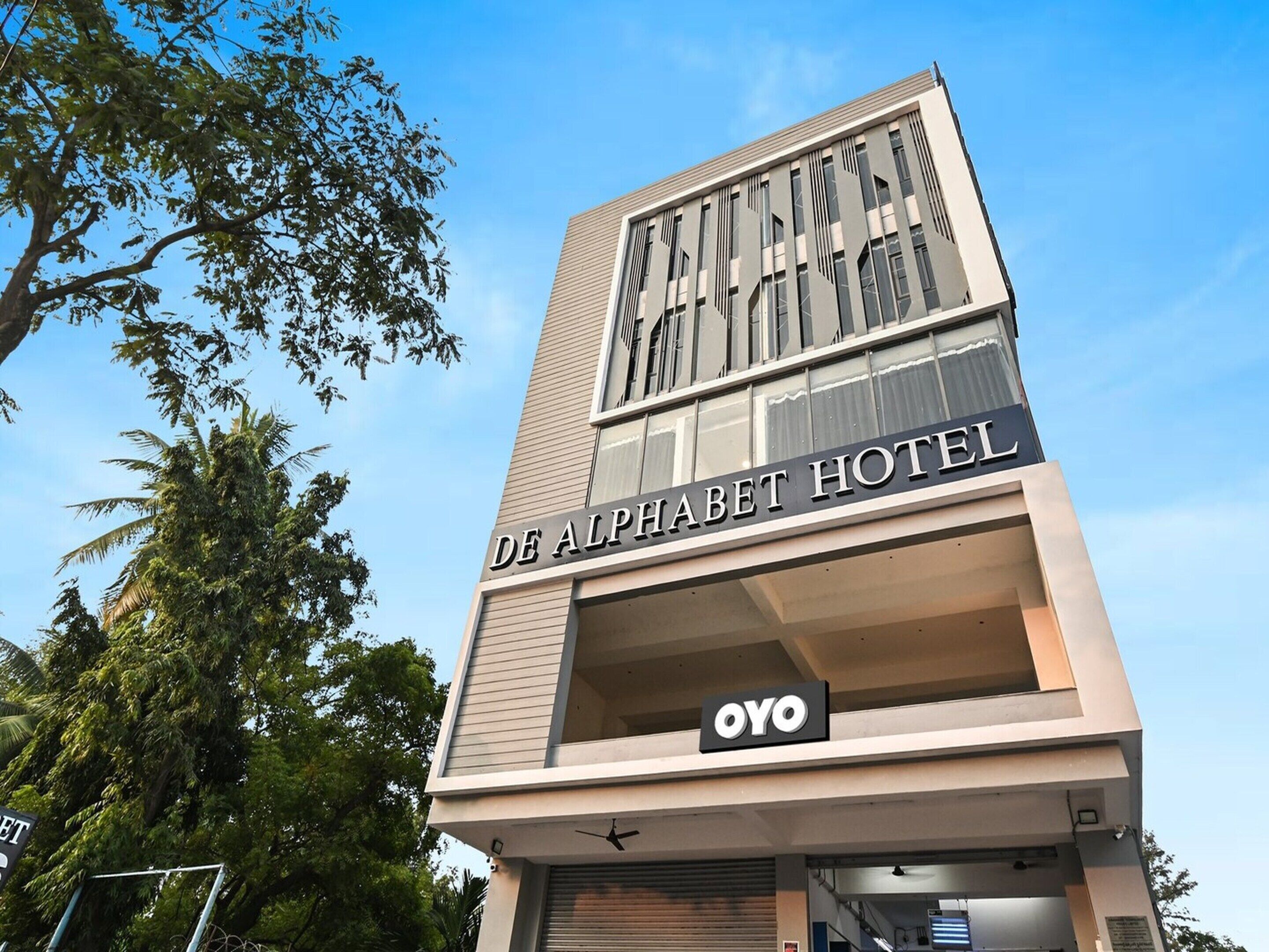 The exterior of De Alphabet Hotel with a modern design, featuring a prominent sign and a logo for OYO.