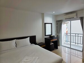 A hotel room with a large bed, a bedside table with a mirror, a small desk, and a view of the outside balcony. - Ahmara Hotel Patong (Patong)