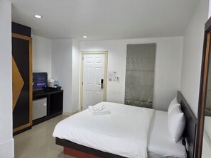 A hotel room with a bed, a desk with a computer, a door, and a window with a curtain. - Ahmara Hotel Patong (Patong)