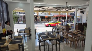 A restaurant with indoor seating, a view of the street, and a red taxi passing by. - Ahmara A Recall Value Hotel Patong, Phuket (Patong)