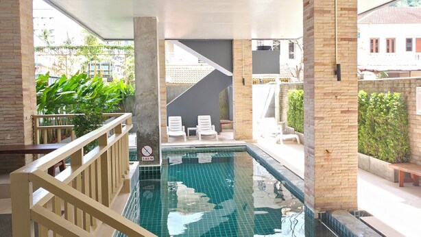 A swimming pool with a tiled floor, surrounded by a wooden railing. There are lounge chairs and a bench near the pool. - Ahmara A Recall Value Hotel Patong, Phuket (Patong)