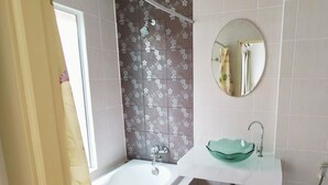 A bathroom with a bathtub, a round mirror, a sink with a green basin, and a black trash bin. - Ahmara A Recall Value Hotel Patong, Phuket (Patong)