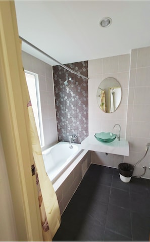 A bathroom with a bathtub, a round mirror, a sink with a green basin, and a black trash bin. - Amara APK Resort and Spa (Patong)