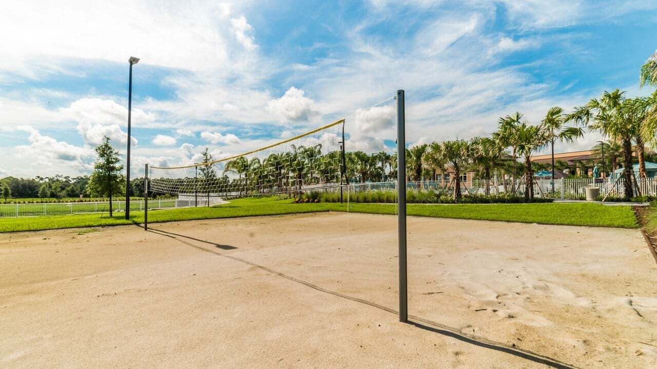 A volleyball court with a net, surrounded by a fence and palm trees.