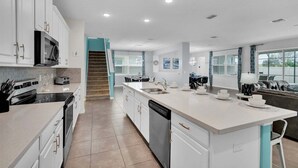 Une cuisine moderne avec des meubles blancs, un îlot central, un four à micro-ondes et un lave-vaisselle.