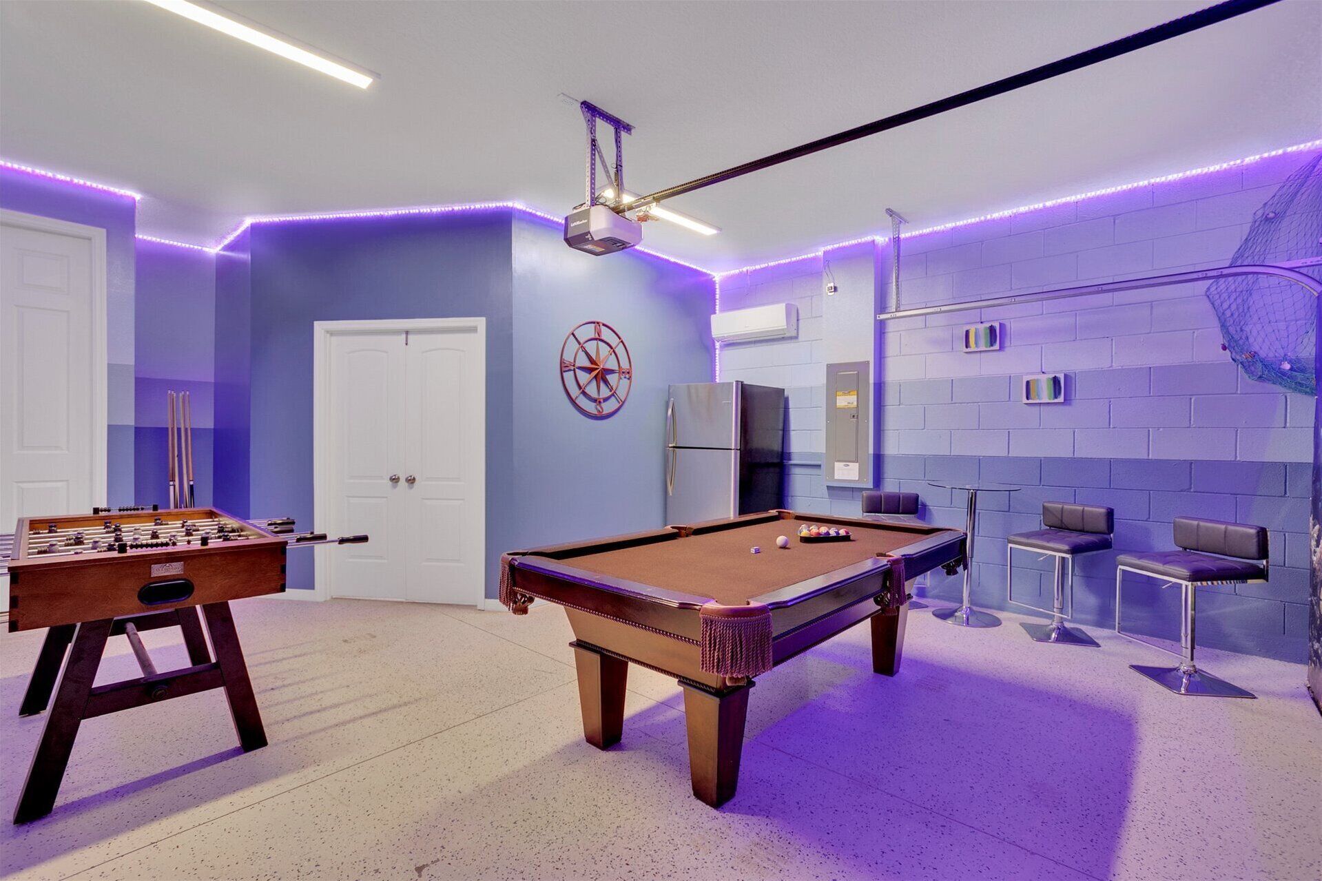 A room with a pool table, foosball table, and seating area with chairs and a couch.