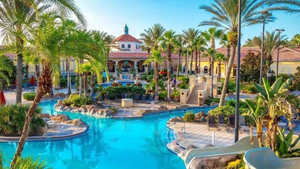 A resort with a central pool, palm trees, and a building with a red roof. - 1307-4-ca-townhome at Regal Palms (Davenport)