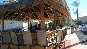 An outdoor bar area with a thatched roof, wicker chairs, and a bar counter. - 1307-4-ca-townhome at Regal Palms (Davenport)