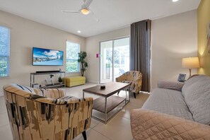 A modern living room with a sofa, armchairs, a coffee table, a TV, and a sliding glass door leading to a balcony. - 1617 Retreat Circle, Clermont, 3 BED (Clermont)