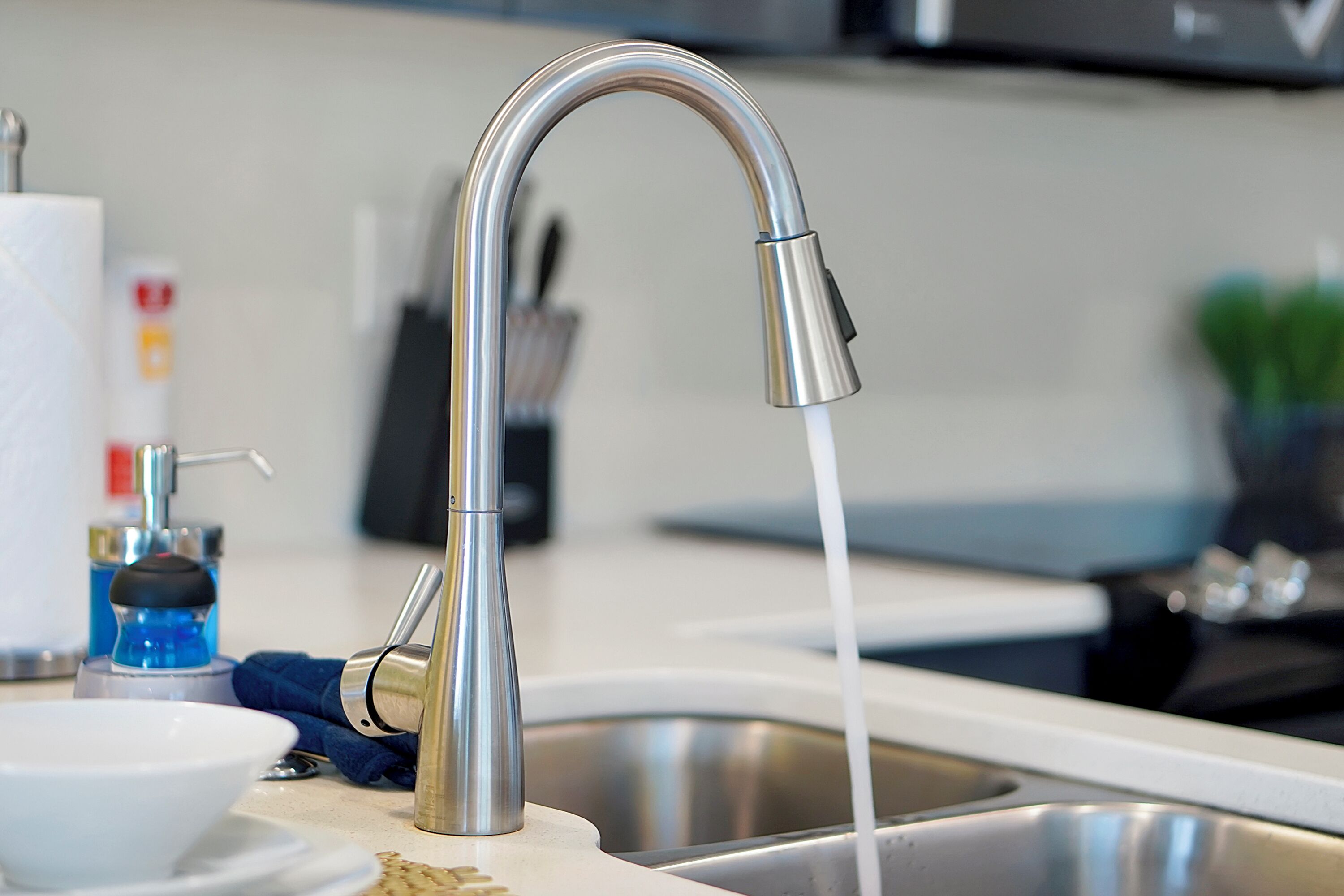 A modern kitchen with a stainless steel faucet, a white sink, and a blue dish soap bottle.