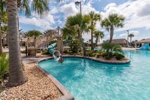 A swimming pool with a water slide, surrounded by palm trees and a thatched-roof building. - 1426 Wexford WAY Davenport, 8bed (Davenport)
