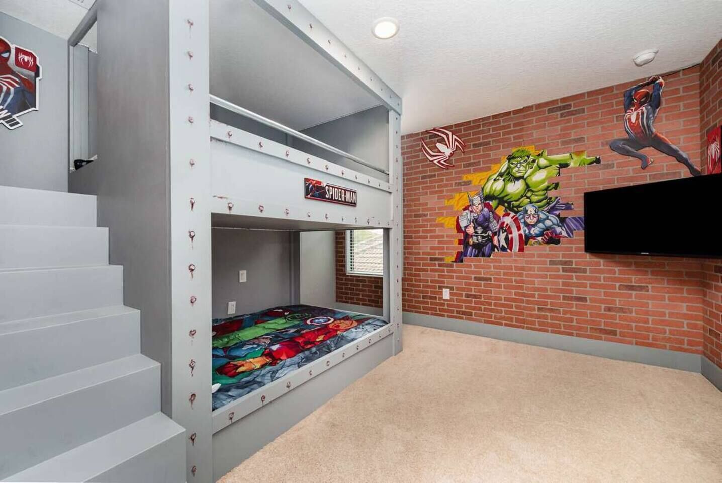 A bunk bed room with a mural of superheroes on the wall and a TV mounted above it.