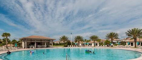 A swimming pool with lounge chairs and palm trees, surrounded by buildings with a covered patio area.