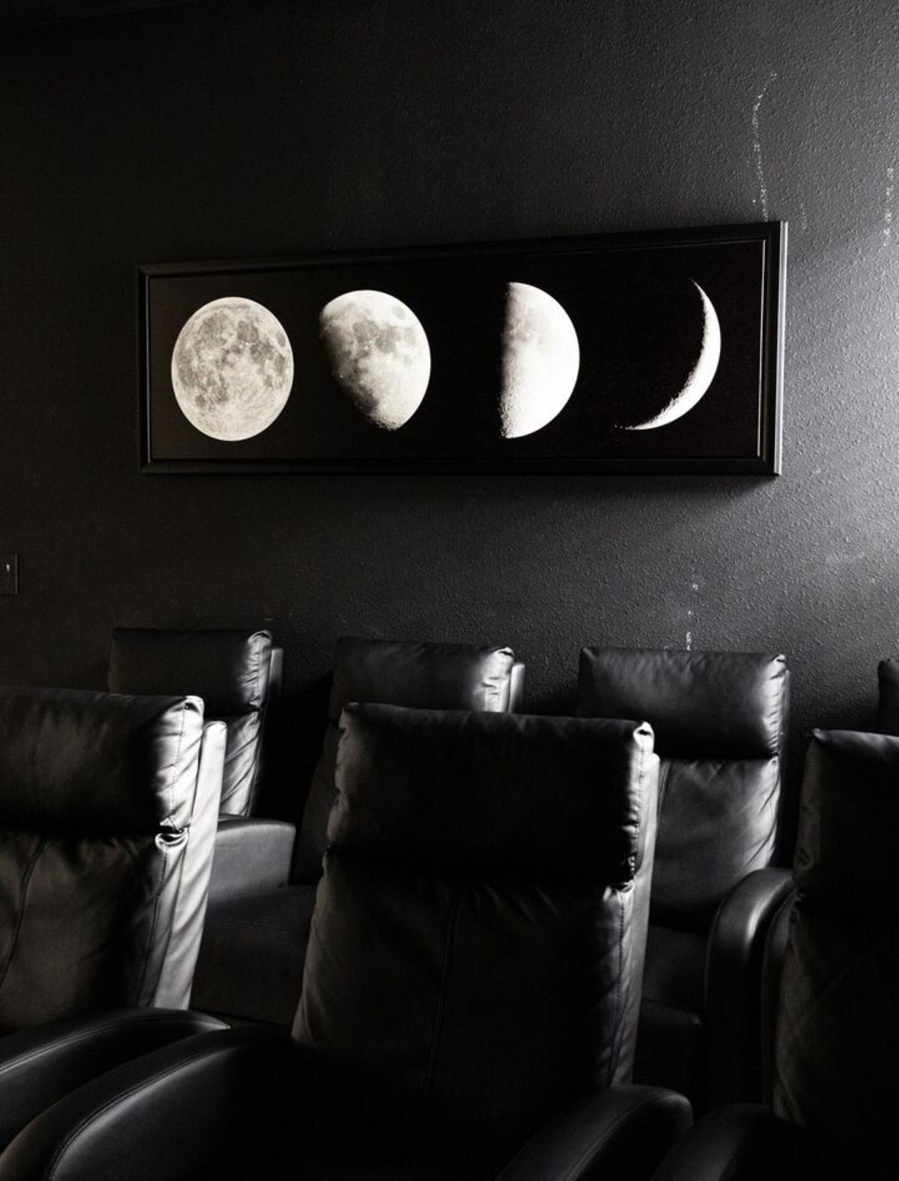 A framed lunar phase artwork above a row of leather chairs in a dimly lit room.