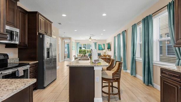 A spacious kitchen with dark wood cabinets, a central island with bar stools, and a view to a dining area. - 520-8-ld-large Movie&game Room (Kissimmee)