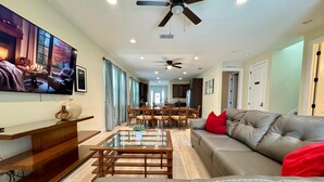 A spacious living room with a grey sofa, a coffee table, and a TV mounted on the wall. - 520-8-ld-large Movie&game Room (Kissimmee)