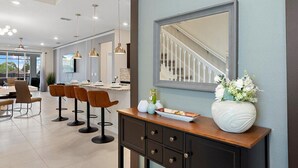 A modern kitchen with a dining area, featuring a large island, bar stools, and a decorative vase. - 3835la · Brand New 7BR in Windsor Island (Davenport)