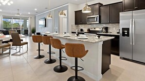 A modern kitchen with a central island, dark cabinetry, stainless steel appliances, and pendant lighting. - 3835la · Brand New 7BR in Windsor Island (Davenport)