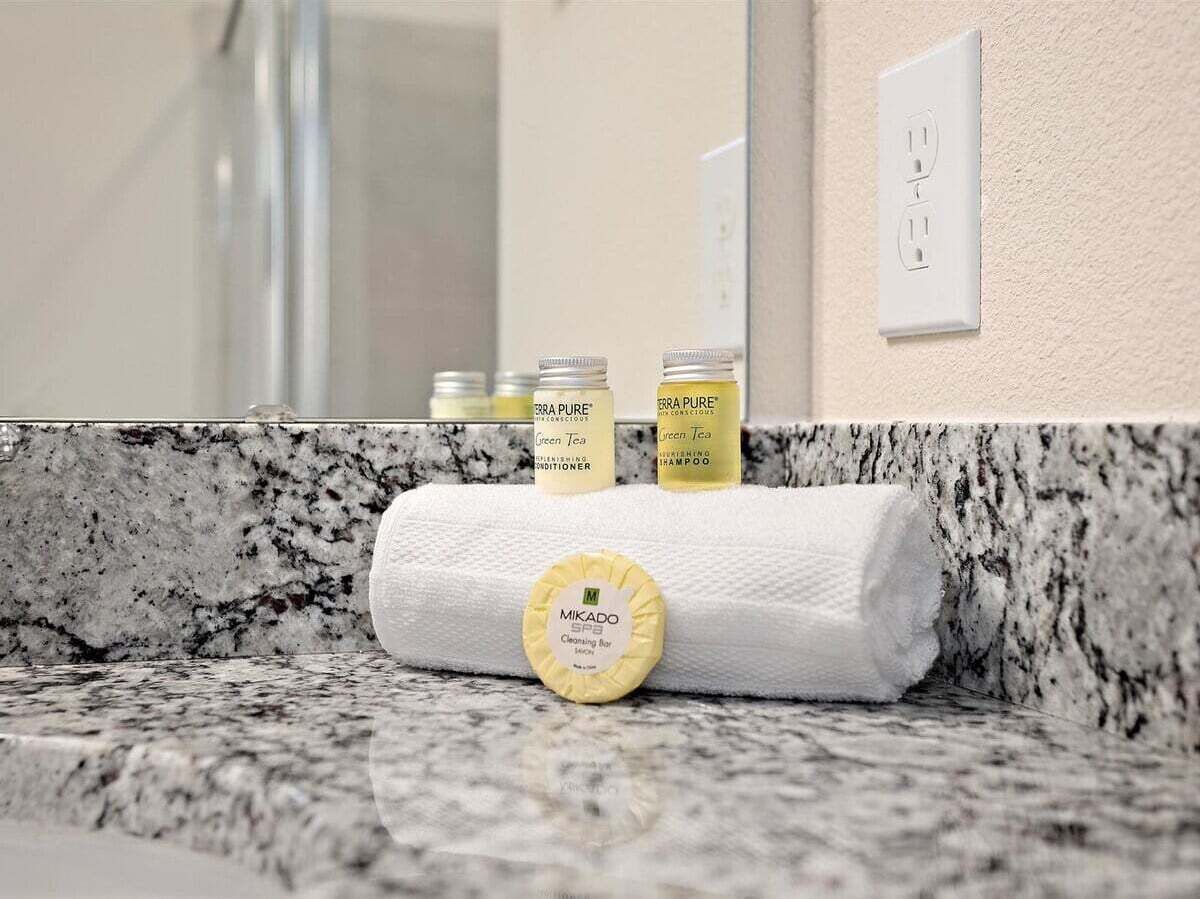 Un baño con encimera de mármol, una toalla y tres botellas de productos de té verde.