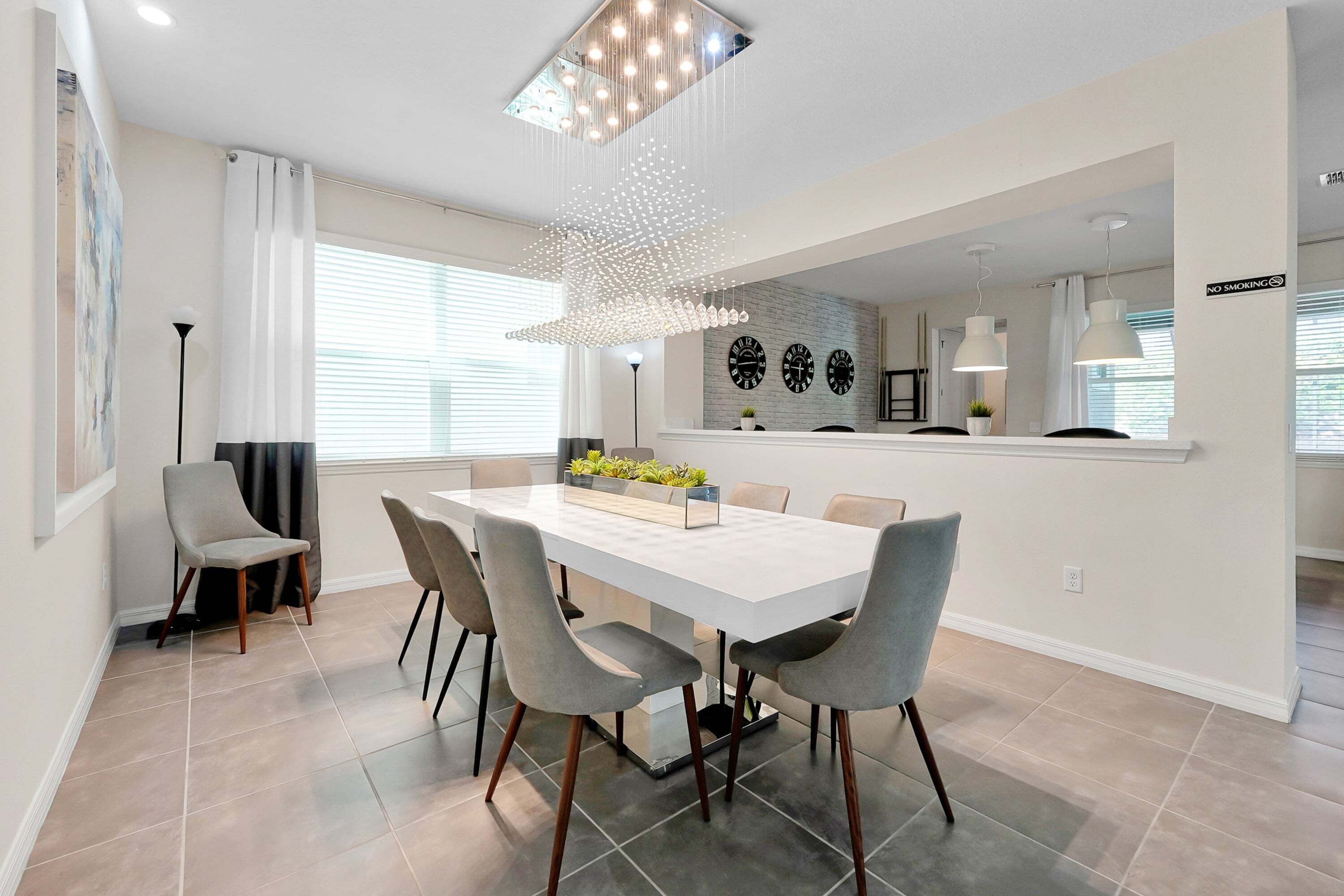 A modern dining area with a white table, grey chairs, a hanging light fixture, and a brick accent wall.