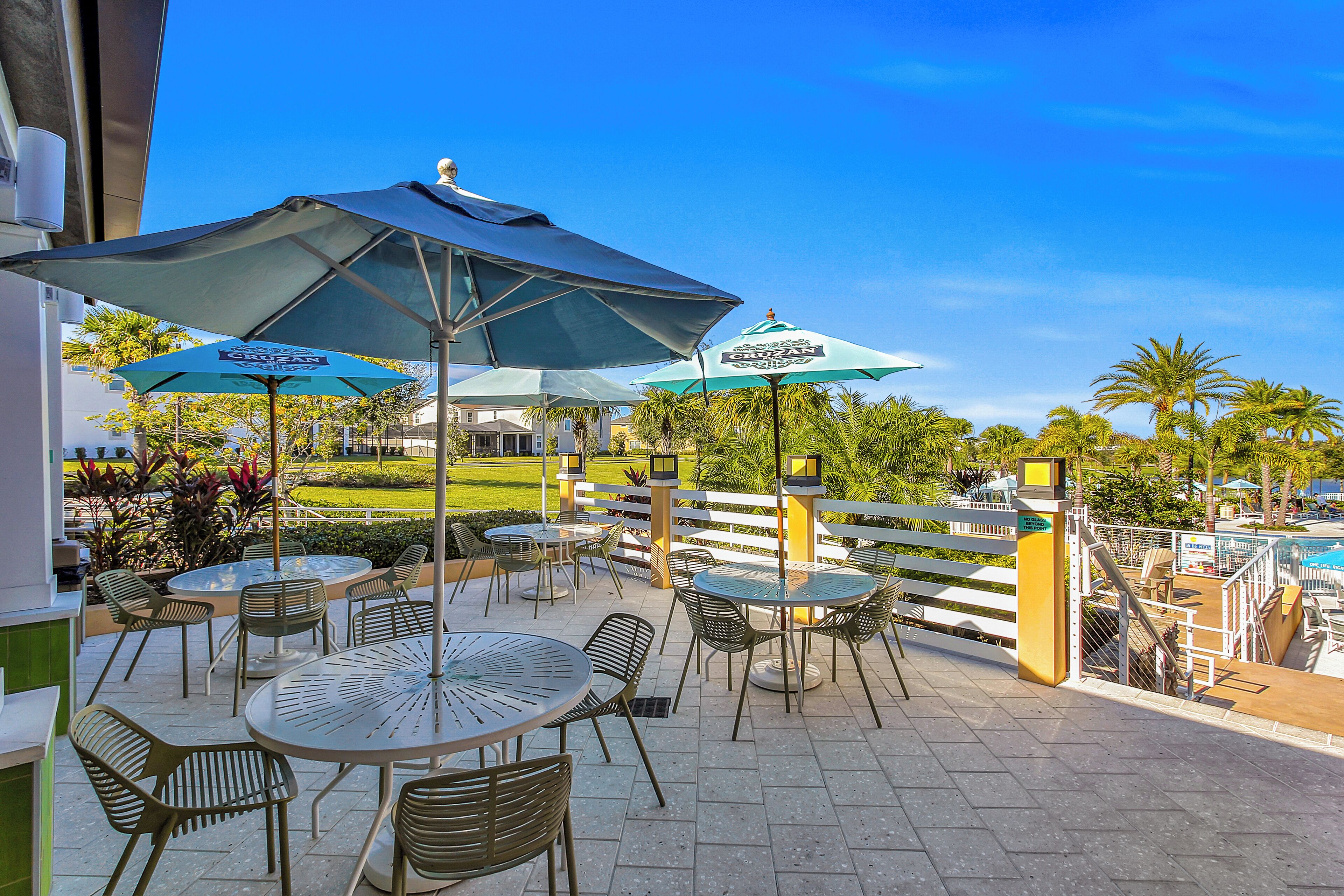 Une terrasse extérieure avec des tables et des chaises, des parasols et une vue sur une piscine et de la verdure.