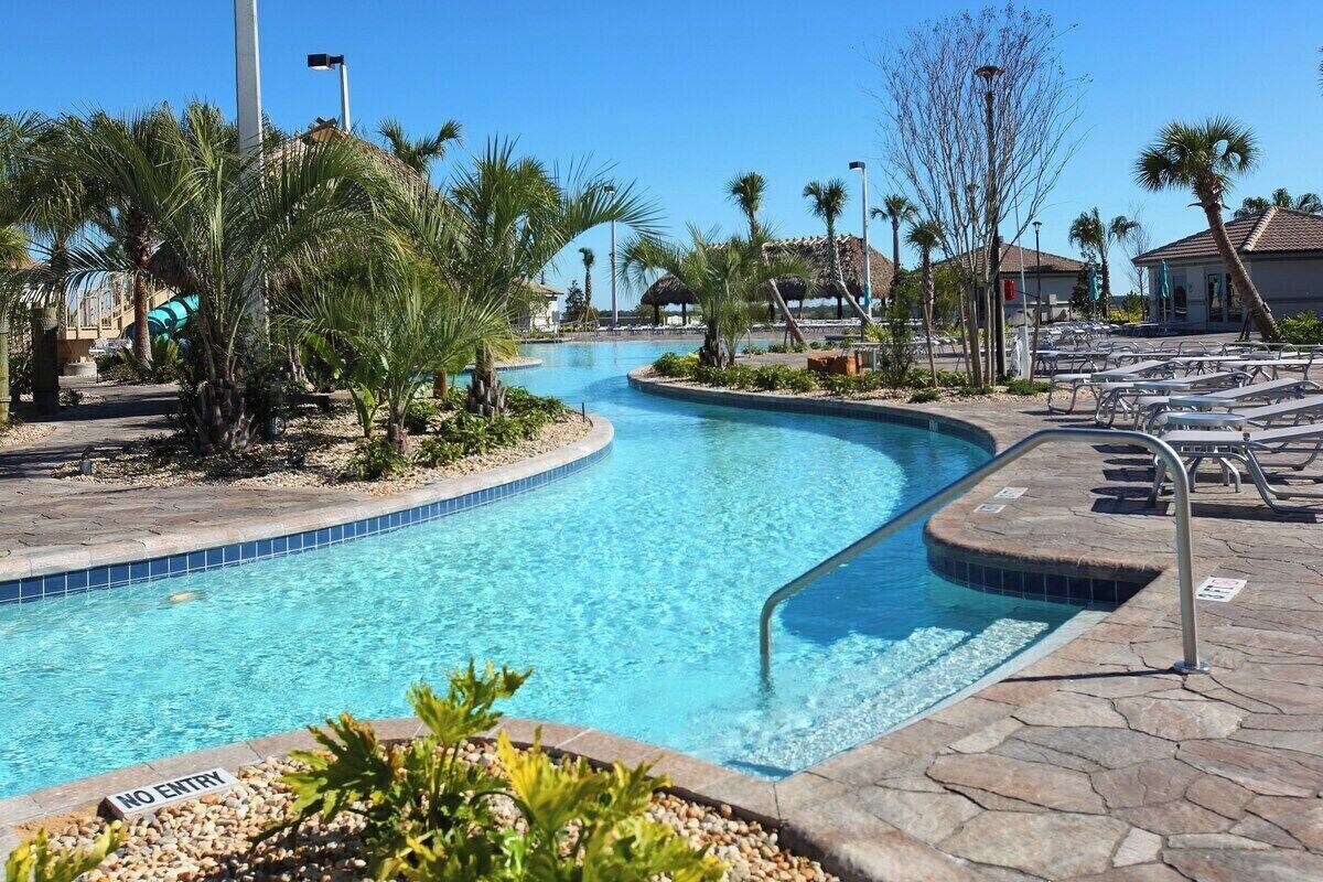 Una piscina de borde curvo, rodeada de palmeras y sillones de descanso.