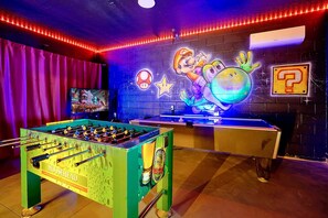 Una habitación con mesa de fútbol de mesa, mesa de billar y un mural con Mario y Bowser.