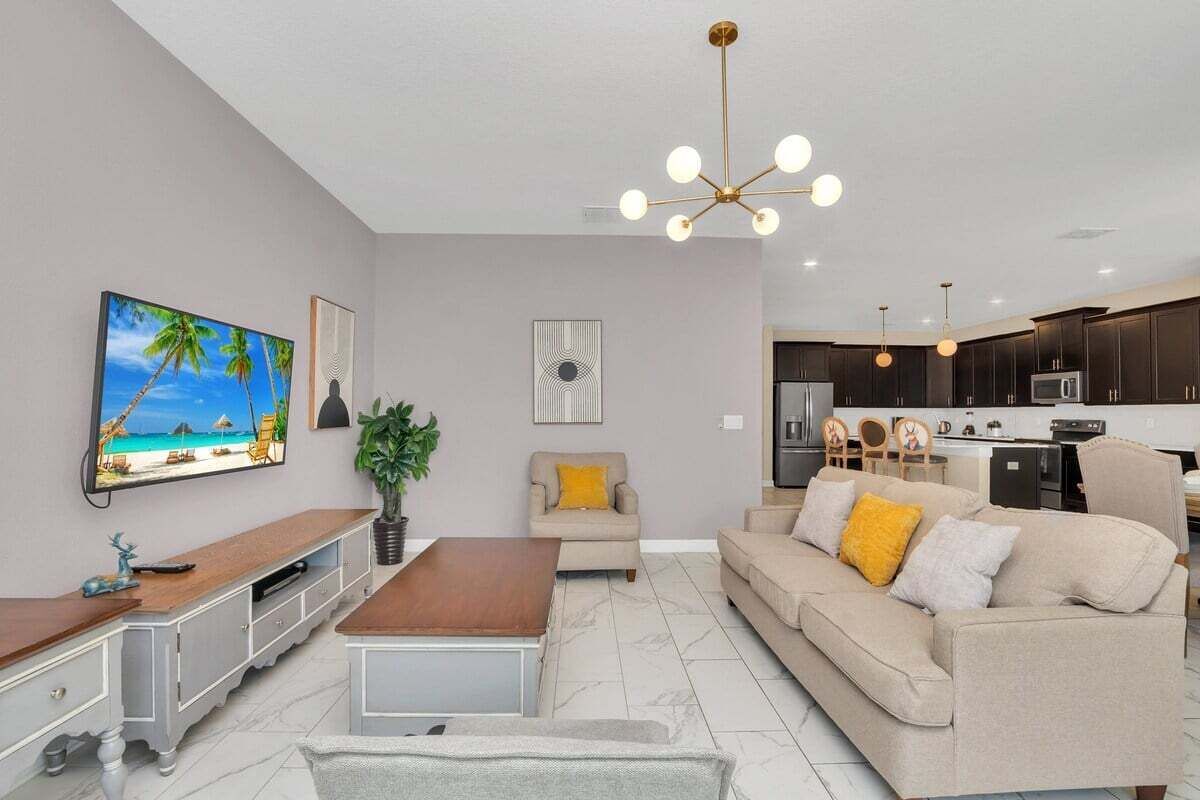 A modern living room with a TV, sofa, coffee table, and a dining area with chairs and a kitchen in the background.